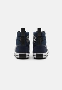 Vysoké tenisky námořnicky modré barvy s polstrovaným svrškem, černými detaily a bílou pruhovanou gumovou podrážkou. Mají kulaté logo a poutko na patě.