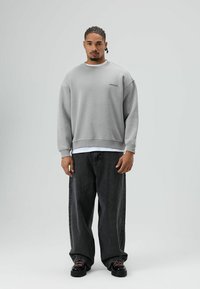 Grijze sweatshirt met verlaagde schouders en geribbelde manchetten, gedragen over een wit T-shirt, gecombineerd met losse zwarte denim jeans en zwarte schoenen.