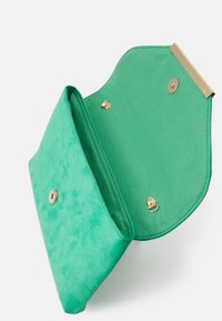 Bolso de mano de ante verde con herrajes dorados. Presenta un cierre de solapa y bolsillos interiores. Textura suave y forma estructurada.