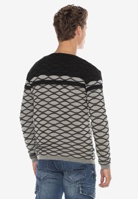 Herren Strickpullover in Schwarz und Grau, mit einem strukturierten Rautenmuster, Rundhalsausschnitt und gerippten Bündchen. Getragen mit blauen Cargo-Hosen.