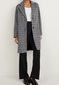 Harmaa ruudullinen takki, jossa on uurrettu kaulus, kaksi nappia ja pitkät hihat, yhdistettynä mustiin leveisiin housuihin ja mustiin loafer-kengiin.