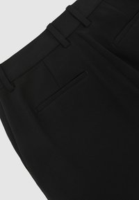 Čierne nohavice s hladkou textúrou, ktoré majú prispôsobený strih, pútka na opasok a jednu zadnú kapsu s jemným otvorom.