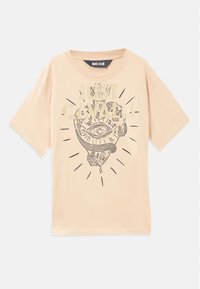 Beige-kesäinen puuvillapaita, jossa on lyhyet hihat, ja jossa on musta ja kultainen graafinen printti tyylitellystä silmästä ja käärmeestä, ympärillä säteileviä viivoja.