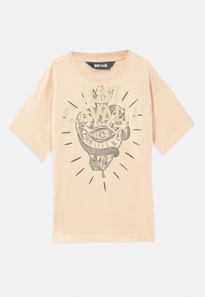 Beige színű, rövid ujjú pamut póló, fekete és arany színű grafikai nyomattal, amely egy stilizált szemet és kígyót ábrázol, a minta körül sugárzó vonalakkal.