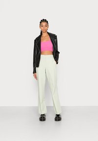 Jaqueta de couro preta, top de malha curto cor-de-rosa, calças largas verde claro e sapatos de plataforma pretos numa modelo contra um fundo simples.