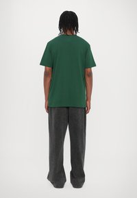 Green short-sleeve t-shirt with a rounded neckline, paired with loose-fitting dark gray trousers. Features a relaxed fit and soft texture.