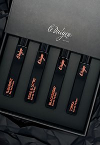 Vier schwarze Parfümfläschchen mit roségoldener Schrift, beschriftet mit "Tuberose", "Feige & Lotus", "Brombeere" und "Tonka", in einer schwarzen Box.