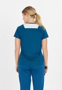 Teal idrottströja med en vit panel på baksidan, korta ärmar och en figurnära design. Bärs med matchande tealbyxor.