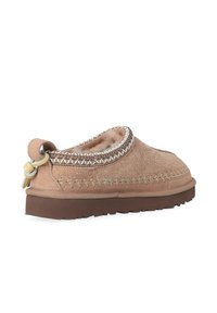 Pantofole in camoscio marrone con tomaia testurizzata, dettagli cuciti e collo rotondo. Presentano una linguetta per facilitare la calzata e una suola in gomma bassa.