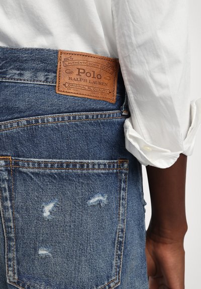 Džinsai su rudą odinį užrašą "Polo Ralph Lauren" prie juosmens. Funkcijos apgadinta detalizacija ir dvi galinės kišenės.