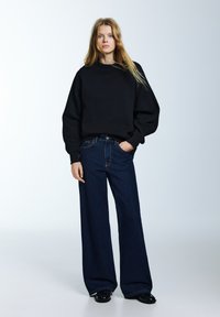 Čierna nadrozmerná mikina s rebrovanými manžetami, doplnená širokými džínsami tmavomodrej farby. Hladká textúra, jednoduchý dizajn a klasický džínový vzhľad.