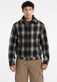 Karirana jakna sa patentnim zatvaranjem u plavoj, crnoj i bež boji, izrađena od teksturiranog materijala, s bočnim džepovima i oštrim kragnom.