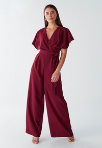 Mono burdeos de pierna ancha con diseño cruzado, mangas cortas, cinturón anudado en la cintura y textura de tela suave. Sin estampados.