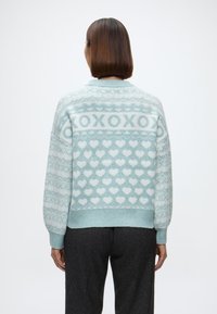 Gaiši zils adīts džemperis ar sirds un "XOXO" rakstiem, ar ribotu apakšmalu un brīvu piegriezumu. Mīksta tekstūra un garas piedurknes.