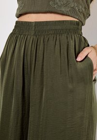 Un gros plan de la taille d'une femme, mettant en valeur une jupe plissée verte avec une taille élastique et une main dans une poche.