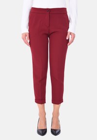 Pantaloni tagliati bordeaux con una consistenza liscia, dotati di chiusura a bottone e orli arrotolati, abbinati a tacchi a punta neri.
