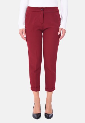 Pantaloni tagliati bordeaux con una consistenza liscia, dotati di chiusura a bottone e orli arrotolati, abbinati a tacchi a punta neri.