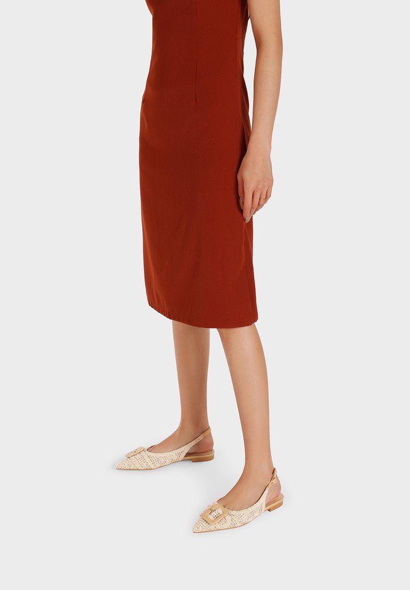 Scarpe slip-on beige con texture intrecciata, punta appuntita, fibbia decorativa e tacco basso, abbinate a un vestito fitted color ruggine.