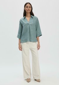 Blusa in lino turchese chiaro con scollatura a V, maniche a tre quarti e vestibilità comoda, abbinata a pantaloni bianchi a gamba larga. Tessuto liscio.