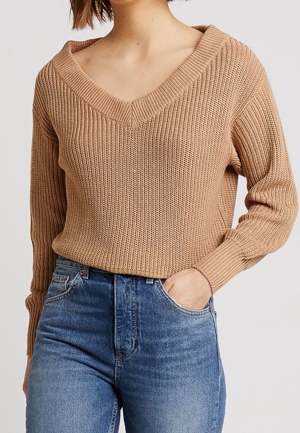 Beige knitted sweater with a V-neck, long sleeves, and ribbed texture, paired with blue high-waisted jeans.