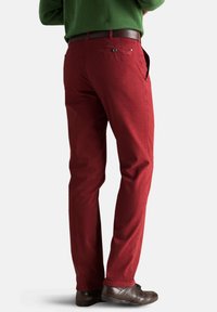 Rote Baumwollhosen mit geradem Schnitt, ausgestattet mit Seiten- und Gesäßtaschen sowie einem braunen Ledergürtel; getragen mit einem grünen Pullover oben.