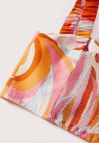 Gros plan sur un tissu multicolore avec des motifs abstraits orange, rose, blanc et bleu et des textures froncées sur les bretelles et le corps du vêtement.