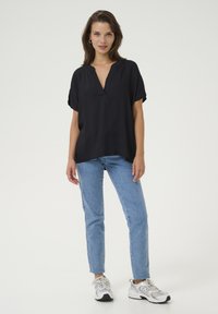 Haut noir à manches courtes avec un décolleté en V, coupe décontractée, texture lisse, associé à un jean bleu clair et des baskets blanches.