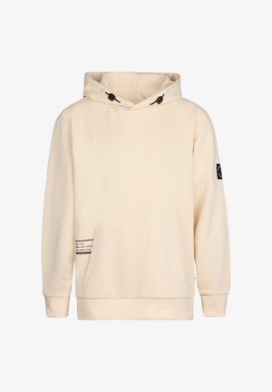 Beige Kapuzenpullover mit verstellbarem Kordelzug, großer Fronttasche und schwarzem Akzentpatch. Kombiniert mit grauen Jeans und weißen Sneakers.
