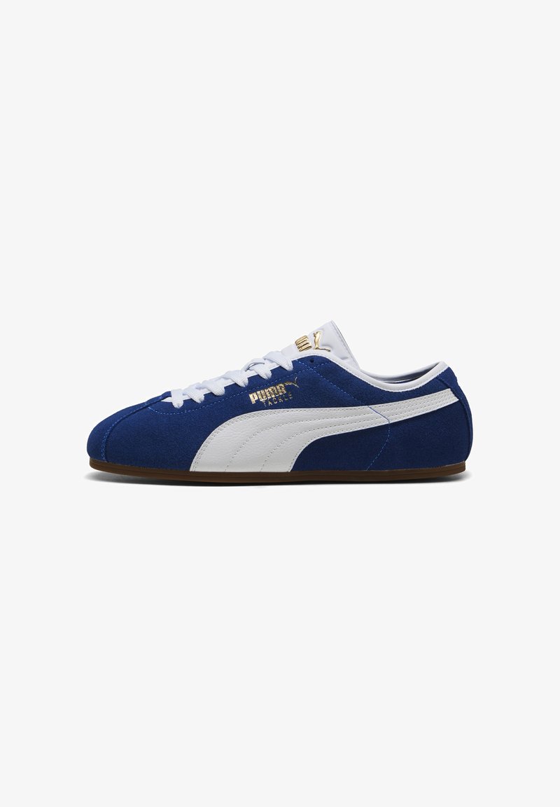 Baskets Puma en daim bleu avec une bande blanche, des lacets blancs et un logo Puma doré sur le côté et la languette, vues de côté.