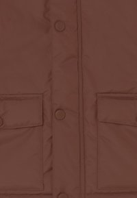 Braune gepolsterte Jacke mit einem schlichten Design, ausgestattet mit Druckknöpfen und zwei Fronttaschen. Das Material wirkt glatt mit einem leichten Glanz.