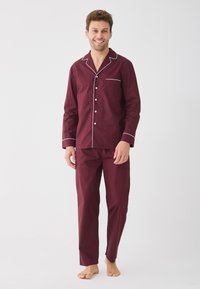 Bordový pyžamový set s bílými detaily, zahrnující dlouhý rukáv s knoflíky a kapsou a odpovídající kalhoty. Vyrobeno z lehkého materiálu.