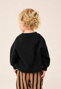 Sweatshirt noir à coupe décontractée, avec un col rond et des poignets côtelés, associé à un pantalon rayé marron et noir.