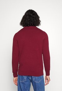 Bordeaux gebreide trui met een ronde hals en lange mouwen. Heeft ribgebreide manchetten en een zoom, gecombineerd met lichtblauwe denim jeans.