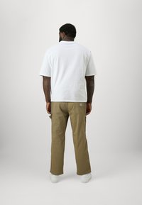 Weißes Baumwoll-T-Shirt mit lockerer Passform, kombiniert mit beigen Cargo-Hosen mit Seitentaschen und weißen Sneakern. Einfaches, funktionales Design.