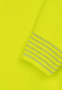 Helles gelbes Strickpullover mit einem markanten Bündchen und silbernen Akzentstreifen. Die Textur ist weich und hat eine glatte Oberfläche.