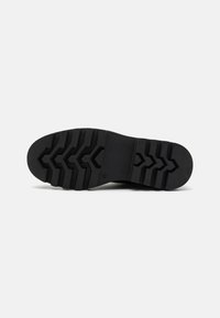 Suela de zapato de goma negra con un patrón de tracción en zigzag y horizontal, y una superficie plana y lisa en el talón.