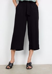 Pantalones recortados de pierna ancha y negros con cintura elástica, hechos de material ligero, con bolsillos laterales y una textura suave.