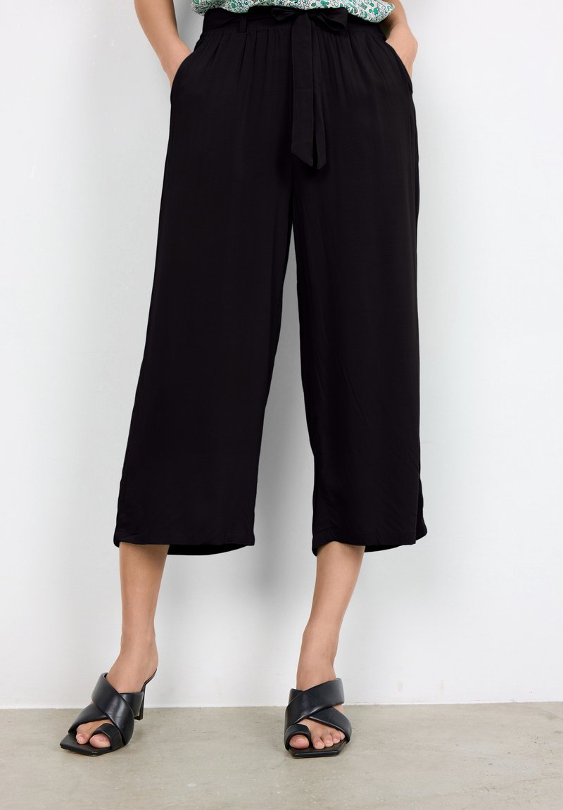 Pantalones recortados de pierna ancha y negros con cintura elástica, hechos de material ligero, con bolsillos laterales y una textura suave.
