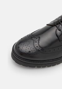 Scarpa nera in pelle con dettagli traforati, punta arrotondata e suola in gomma spessa. Design con lacci e sottili dettagli di cucitura.