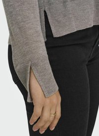 Maglione grigio chiaro con polsini a costine e fessure laterali, abbinato a pantaloni neri. Il materiale sembra morbido con una texture liscia.