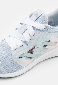 Baskets de sport bleu clair avec une tige en tricot texturé, des lacets blancs, des accents argentés et un design latéral à motifs subtils.