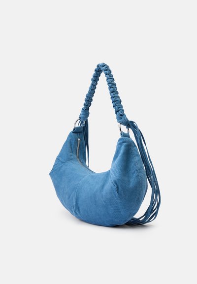 Blauwe corduroy handtas met een afgeronde, asymmetrische vorm. Voorzien van een gevlochten handvat en een ritssluiting aan de zijkant. De textuur is zacht met fijne ribbels.