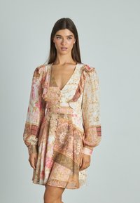 Sukienka ma kwiatowy i wzorzysty design w różowych i złotych odcieniach. Długie rękawy, falbany oraz dopasowany biust z detalami guzików.