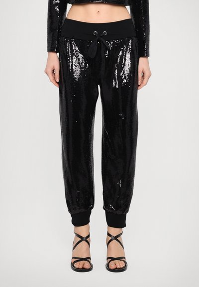 Des joggers en sequins noirs présentent une large ceinture noire, un cordon de serrage et des poignets ajustés ; des sequins brillants créent une surface texturée.