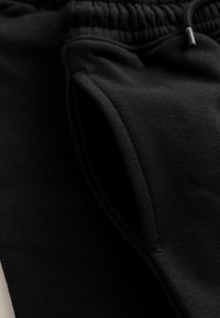 Mustat collegehousut, jotka on valmistettu pehmeästä materiaalista, ominaisuuksinaan joustava vyötärönauha, sivutaskut ja sileä pinta kaksoissaumoilla.