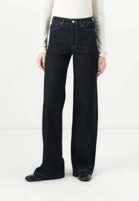 Weite, dunkle Jeans mit hoher Taille, ausgestattet mit klassischer Naht und fünf Taschen, kombiniert mit einem eng anliegenden, weißen Langarmoberteil.