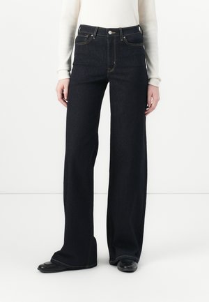 Bredde ben mørk denim jeans med høy midje, med klassisk søm og fem lommer, iført en tettsittende hvit langermet topp.