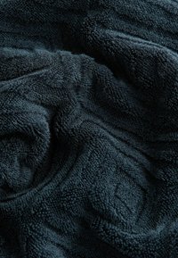 Tela de toalla de rizo de color azul oscuro con un patrón texturizado. Fibras suaves y esponjosas crean una apariencia acogedora y una sensación táctil.