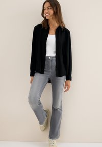 Chemise noire à col, associée à un jean gris clair et des baskets beiges. La chemise a des manches longues et une coupe décontractée.