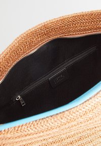 Sac cabas en paille tissée avec un extérieur marron clair et un intérieur noir. Comprend une poche zippée et une bordure bleu clair le long du bord supérieur.